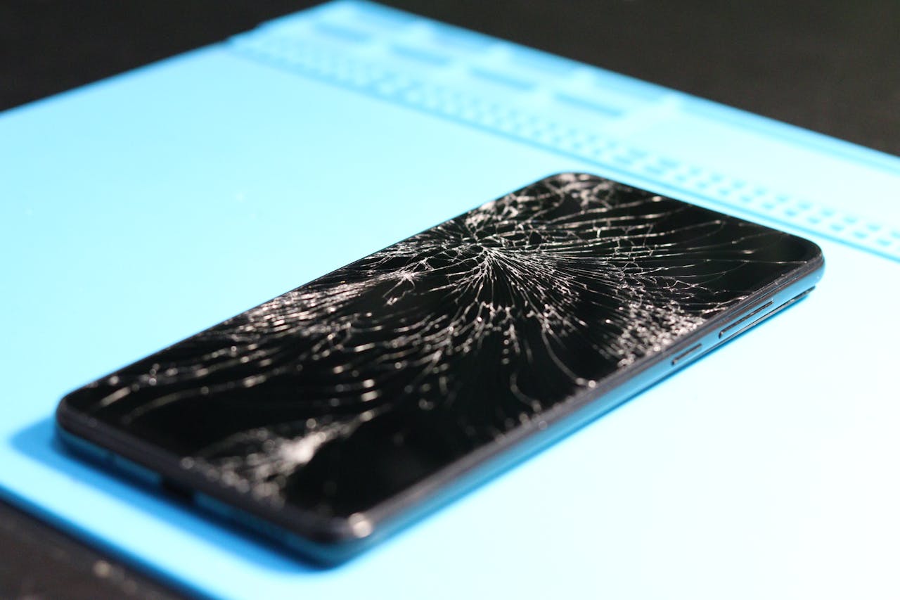 about-01 A cracked smartphone screen on a repair mat highlights technology mishaps.